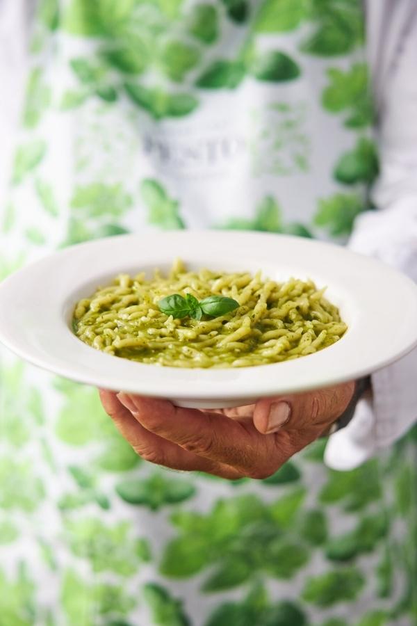 Mensch hält einen Teller Pesto Genovese mit Pasta vor sich