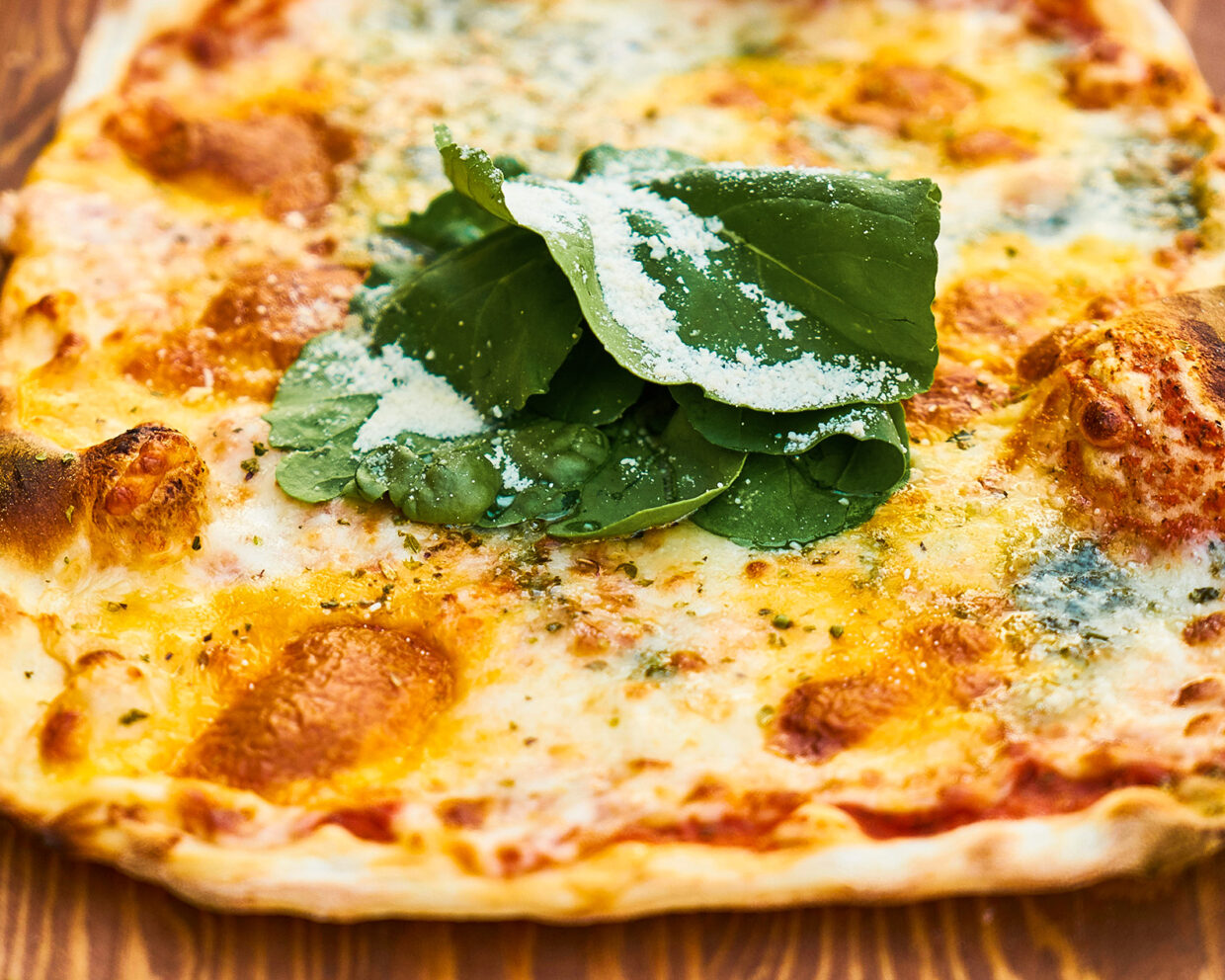 eine glutenfreie Pizza liegt fertig gebacken auf einem Holzbrett, sie ist Parmesan und Basilikum garniert, daneben liegen Tomaten, Knoblauch und Pilze