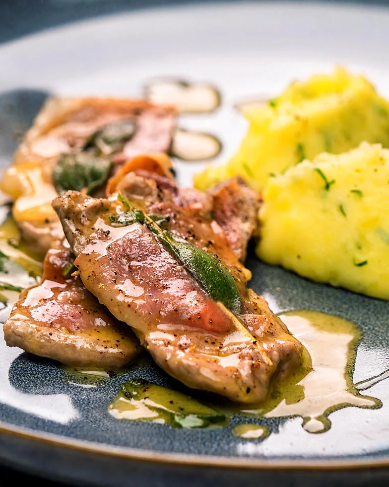 Saltimbocca Romana serviert mit Kartoffelpüree auf einem blauen Teller