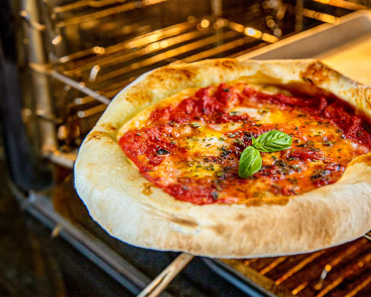 eine frisch gebackene Pizza wird mit Hilfe eines Pizzaschiebers aus dem heimischen Backofen gehoben