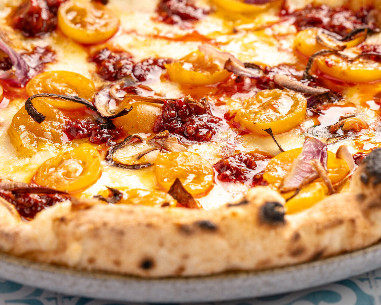 die saftige Oberseite einer neapolitanischen Pizza belegt mit Nduja, gelben Tomaten und Fior di Latte ist zu sehen