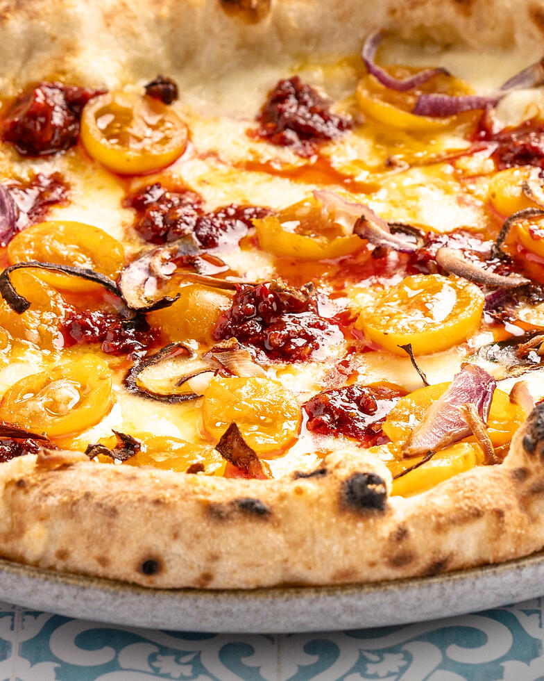 die saftige Oberseite einer neapolitanischen Pizza belegt mit Nduja, gelben Tomaten und Fior di Latte ist zu sehen