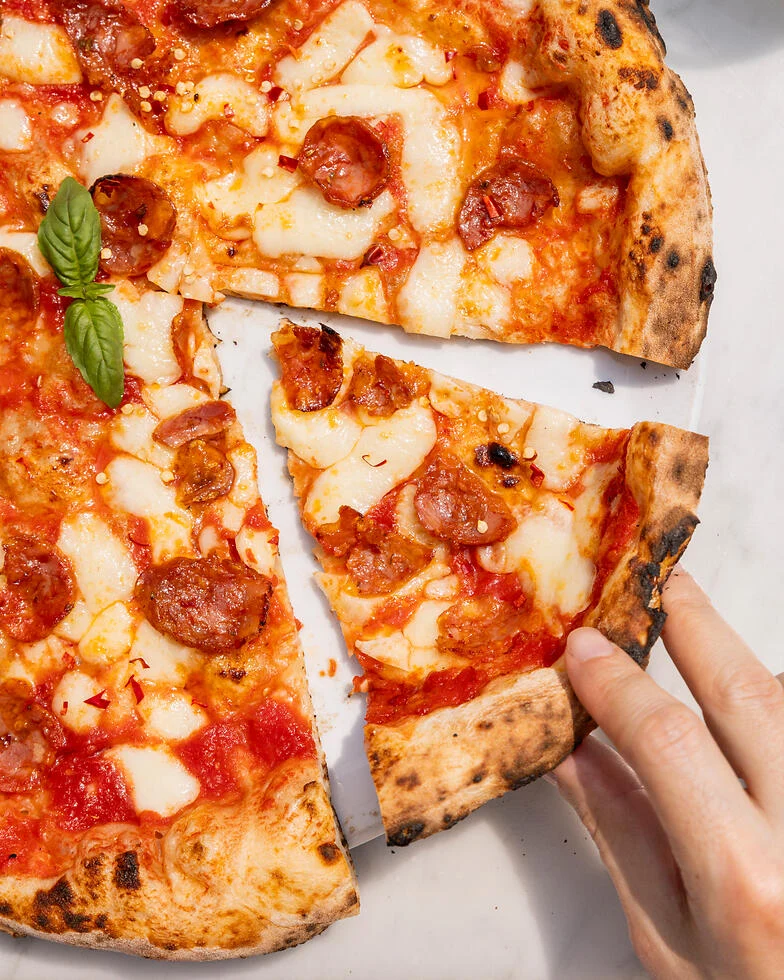 Nahaufnahme einer Hand, die ein Stück frisch gebackener Pizza Diavola nimmt