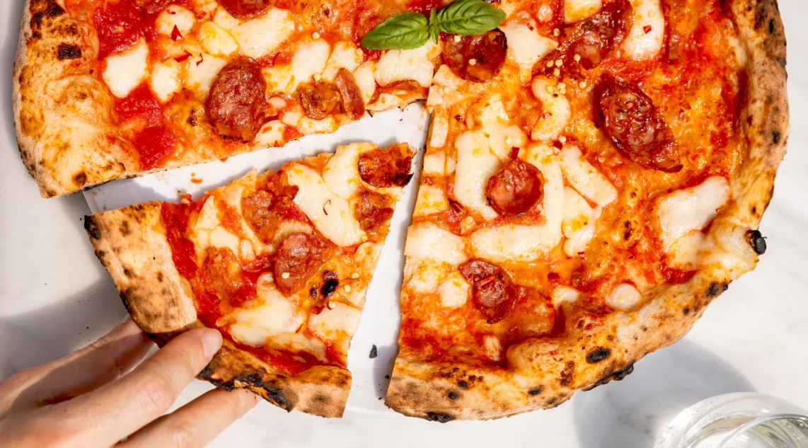 Nahaufnahme einer Hand, die ein Stück frisch gebackener Pizza Diavola nimmt