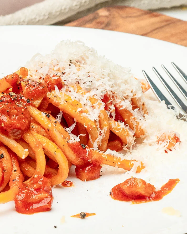 auf einem weißen Teller ist eine frische Portion Bucatini Amatricana angerichtet, am Bildrand liegt eine Gabel