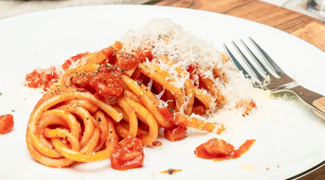auf einem weißen Teller ist eine frische Portion Bucatini Amatricana angerichtet, am Bildrand liegt eine Gabel