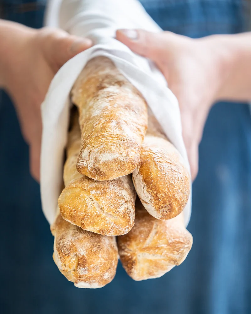 eine Person hält fünf frische Ciabatta-Brote in den Händen
