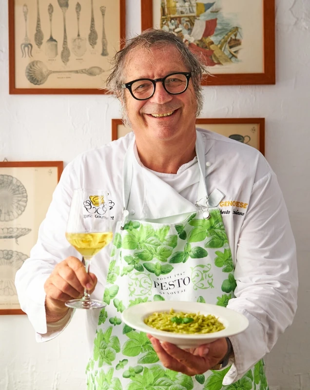 Roberto Panizza lächelt in die Kamera und hält einen Teller mit Trofie al Pesto Genovese