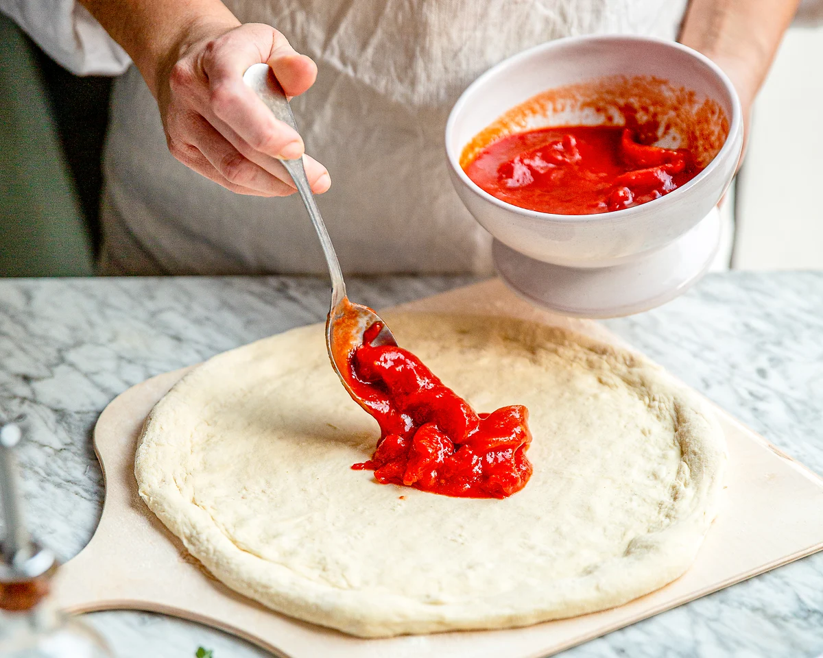 Rohe San-Marzano-Tomatensauce wird auf Pizzateig verteilt