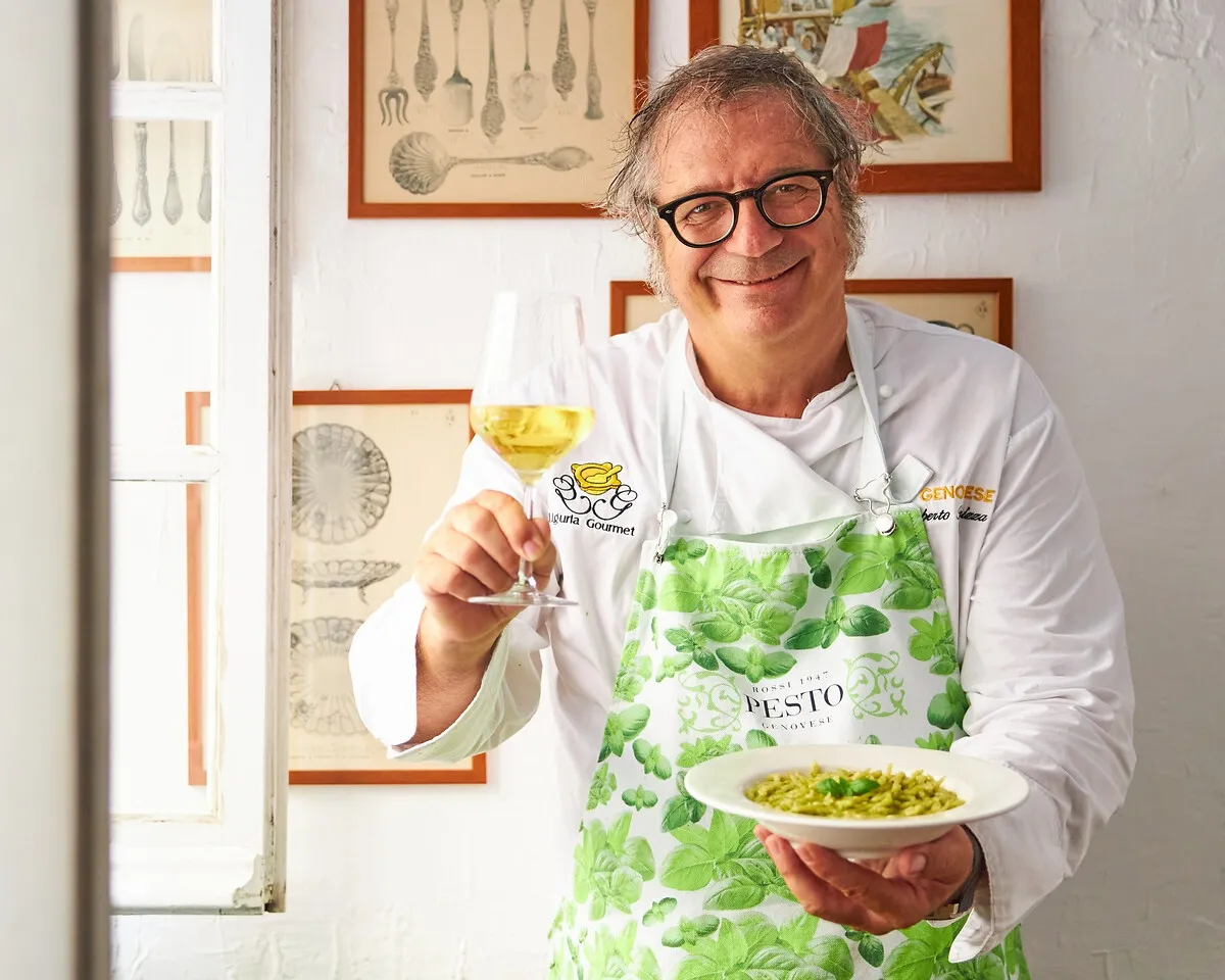 Roberto Panizza lächelt in die Kamera und hält einen Teller mit Trofie al Pesto Genovese